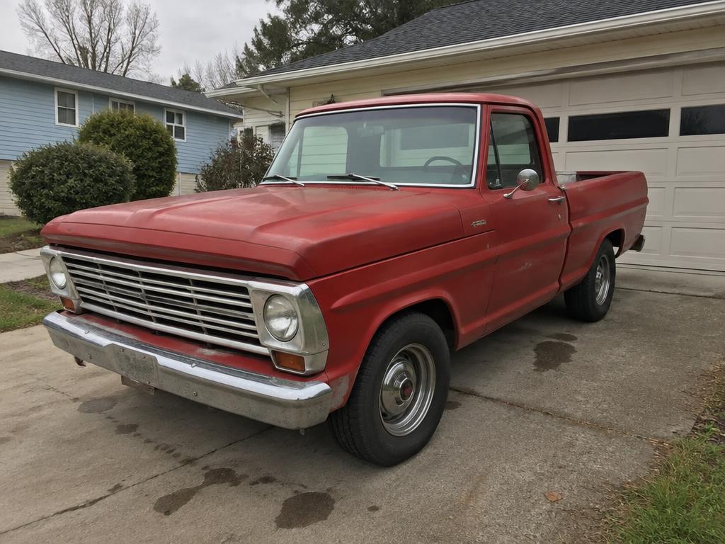 Restored red classic Ford F-100 pickup parked by a barn